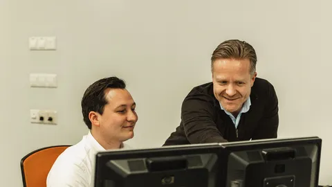 Twee KIN-makelaars kijken lachend samen naar een beeldscherm