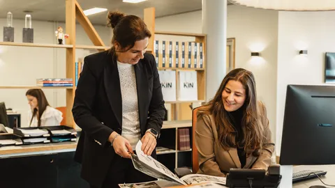 Twee medewerksters bekijken samen een brochure aan het bureau