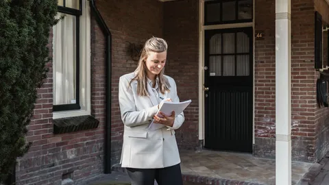 Makelaar met papieren in de hand voor de deur van een woning
