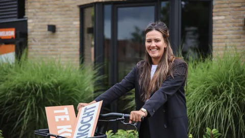 Medewerkster met een fiets en een verkocht-bord voor het kantoor