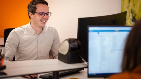 Lachende medewerker achter zijn bureau met beeldscherm